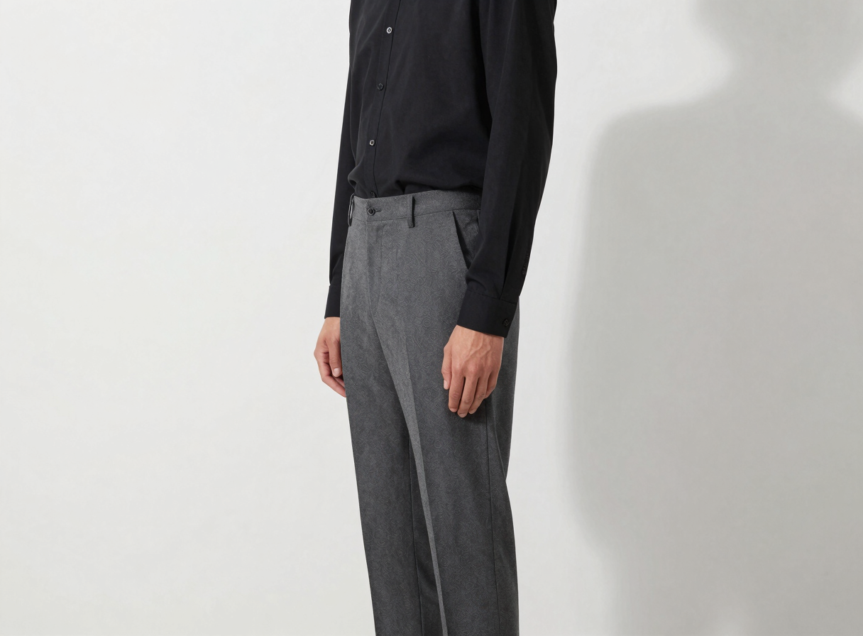 Side profile of a man wearing structured charcoal grey trousers and a minimalist black button-up shirt, standing against a clean white gallery wall, sharp architectural shadows