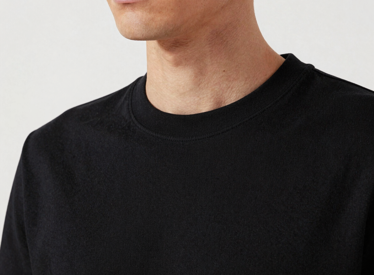 Close-up of a premium structured black cotton t-shirt collar on a model, highlighting the thick fabric texture and clean stitching, soft studio lighting, minimalist desaturated tones